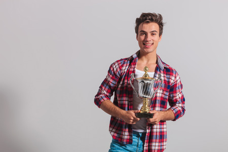 happy young casual man holding a trophy cup and smiles on grey backgroundの写真素材