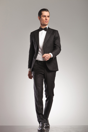walking elegant man in tuxedo is looking up to side on grey studio backgroundの写真素材
