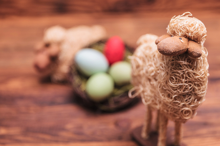 easter toy sheep in fron of egg basket on old wood backgroundの写真素材