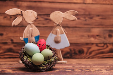 easter eggs basket in front of wooden rabbits on old wood background