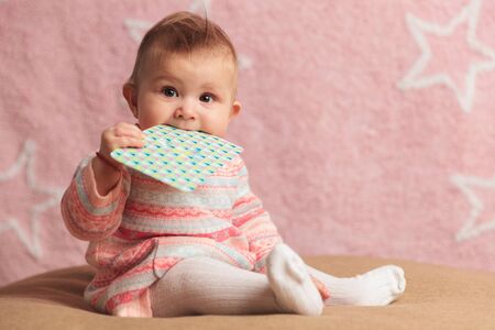 cute little baby girl eating on a card against pink backgroundの写真素材