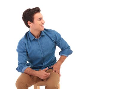 seated casual young man laughing and looks to side on white backgroundの写真素材
