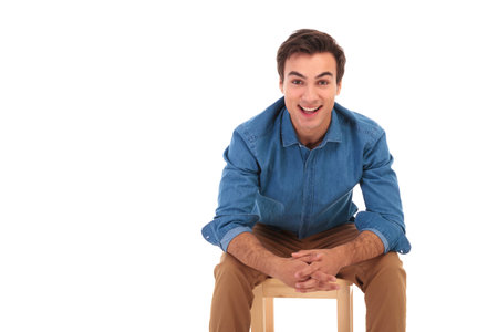 smiling casual man resting elbows on knees while sitting on chair on white background