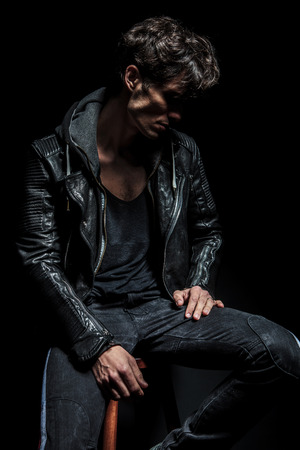 side view of a punk looking down while sitting on chair on black backgroundの写真素材