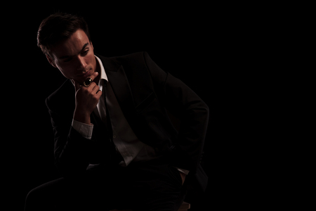 man in tuxedo wearing big ring in thinking on black background, while sitting on chairの写真素材