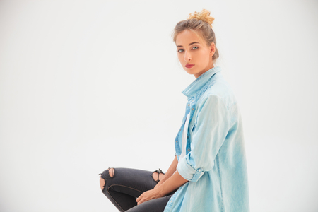 side view of a casual woman wearing man's shirt and looks at the camera while sitting in studioの写真素材