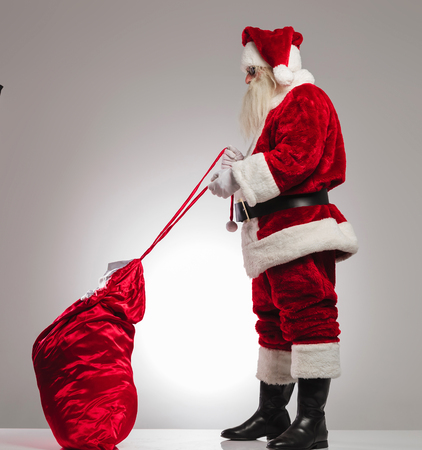santa claus tyeing his presents bag on grey backgroundの写真素材