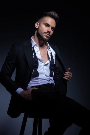 sexy man in tuxedo pulling his collar while sitting on stool in studioの写真素材