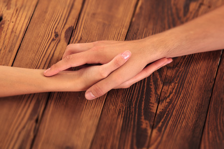 Close up on a man and a woman holding hands on  a wooden tableの写真素材