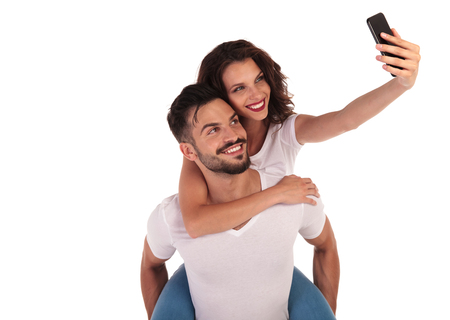 casual happy couple taking a selfie picture with their phone on white backgroundの写真素材
