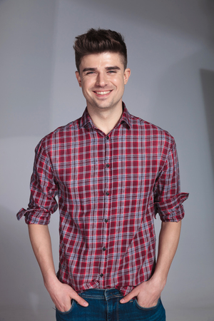 relaxed laughing casual man with red checkers shirt standing with hands in pockets near a grey wall backgroundの写真素材