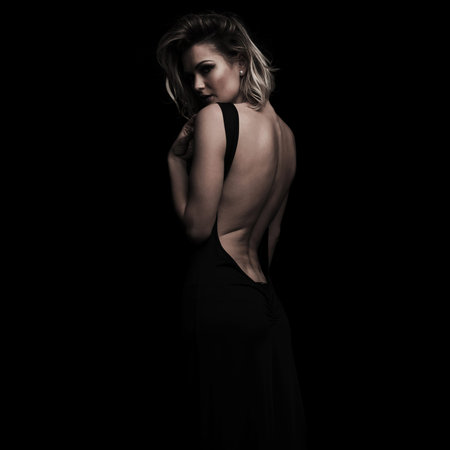 side view of seductive woman wearing an open back dress while standing on a black background