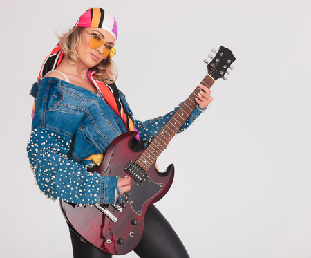 woman rock star with colorful outfit playing the electric guitar while standing on light gray backgroundの写真素材