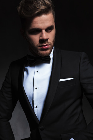 portrait of handsome young man wearing a black tuxedo looking to side on black backgroundの写真素材