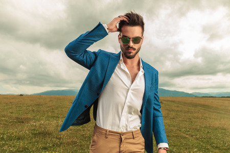 smart casual man with sunglasses fixing his hair in a grass field, portrait pictureの写真素材