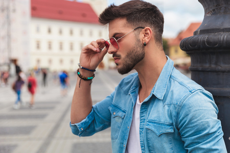 sexy casual man fixing sunglasses outside in the city looks to side, portrait pictureの写真素材
