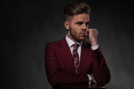 portrait of pensive elegant man resting his hands on wooden chair and looking to side while standing on grey wallpaper backgroundの写真素材