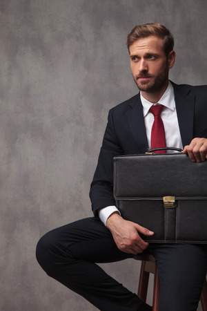 young businessman looks to side while waiting for interview, seated on a cheir in studioの写真素材