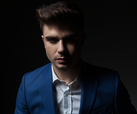 portrait of handsome young man wearing a blue suit while standing on black backgroundの写真素材