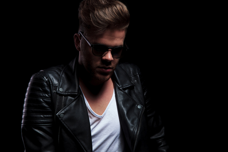 portrait of attractive young man in leather jacket looking down while standing on black backgroundの写真素材