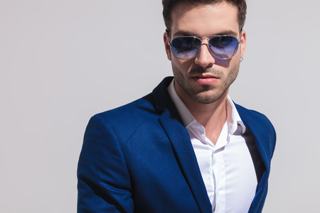 closeup portrait of a sexy young elegant man in blue suit and sunglasses looking at tne camera on grey backgroundの写真素材