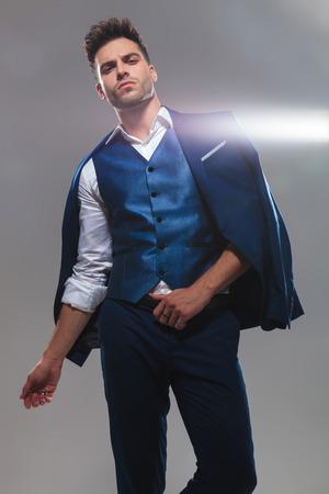 portrait of proud elegant man posing with suit on shoulders while standing on light grey backgroundの写真素材