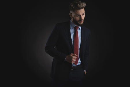 portrait of seductive man holding pockets looking down to side while standing on black backgroundの写真素材