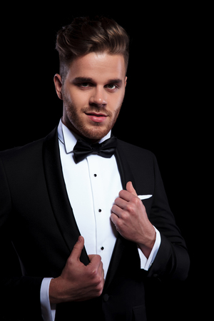 front view of young elegant man puliing his tuxedo's collars while looking awayの写真素材