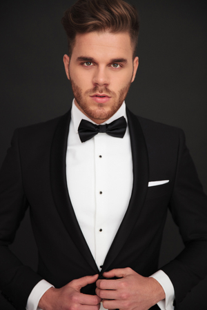 portrait of young groom looking into the camera and buttoning his coat on black backgroundの写真素材