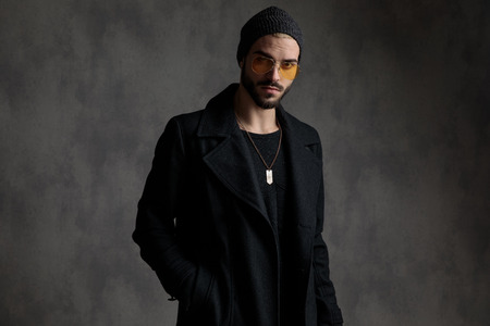 Attractive man wearing modern clothes and a pair of shades standing with a hand in his pocketの写真素材