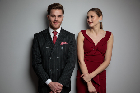 smiling elegant man and woman leaning against grey wall in studioの写真素材