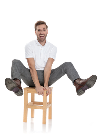 funny playful casual man celebrates while sitting on a chair with legs in the air on white backgroundの写真素材