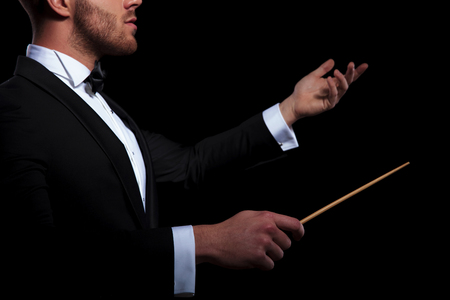 side view of young musician conducting using a stick and gesturing on black backgroundの写真素材
