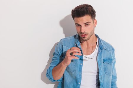 Attractive man holding his pair of shades against his bottom lip while looking at the camera on a light backgroundの写真素材