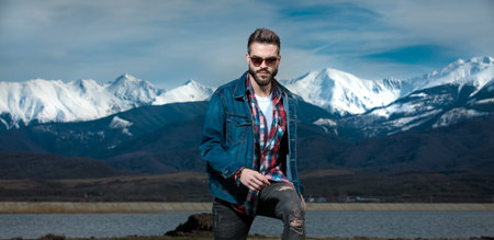happy young casual man stepping up in the outdoors, against lake, mountains and blue coudy sky...