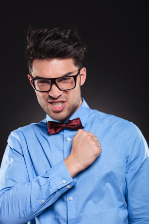 Confident young man standing and staring at camera with his fist clenched while wearing glasses and suit on grey studio backgroundの写真素材