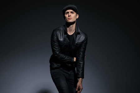 Artistic man posing as powerless and looking to the camera while wearing a cap and black leather...