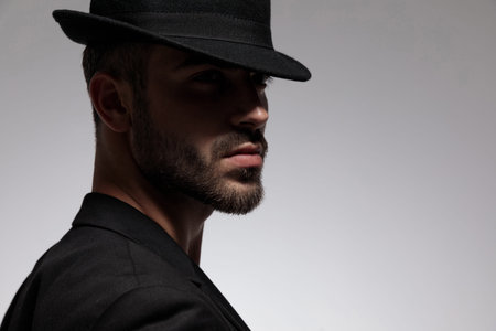 Close up of a handsome casual man wearing a black jacket and hat whille standing on gray studio...