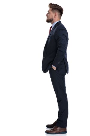 Side view of a confident businessman holding his hands in his pocket while wearing a blue suit and standing on white studio backgroundの写真素材