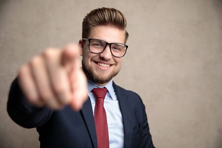 Positive businessman pointing and laughing while wearing a blue suit and sunglasses, standing on soft wallpaper backgroundの写真素材