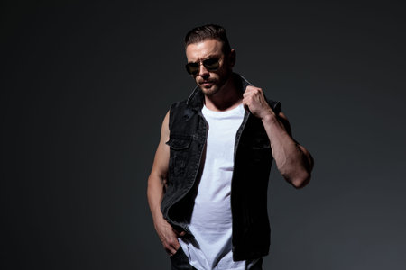 cool guy with hand in pocket fixing his collar on dark grey backgroundの写真素材