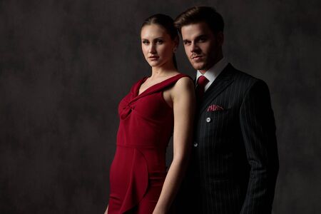young stunning couple cutely standing side by side looking ahead with a pensive expression on their face on gray studio backgroundの写真素材