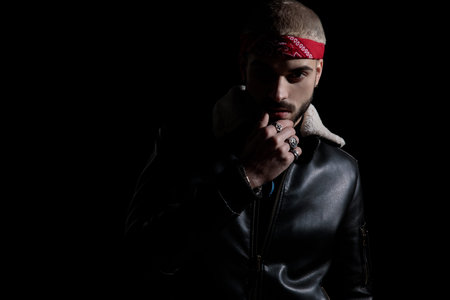 Thoughtful young man dressed as a biker, with a leather jacket and red headband, looking to the...