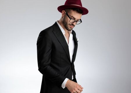 side view of a fine formal business man wearing a black suit,hat,glasses,ring standing and looking down sad on gray studio backgroundの写真素材