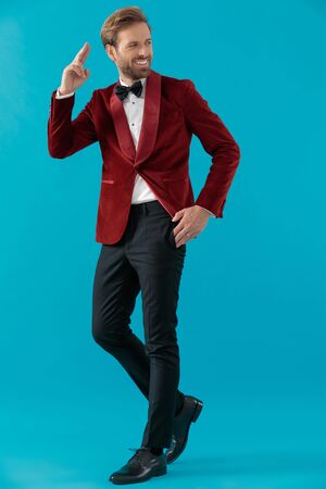 happy elegant man in red velvet tuxedo, walking and looking to side, military saluting on blue background, full bodyの写真素材