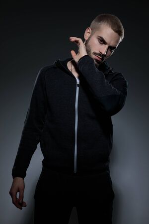 young fashion guy wearing gym suit, holding hands and touching beard, standing isolated on grey backgroundの写真素材