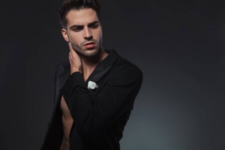 dramatic cool guy holding hand behind neck in a fashion pose and looking to side, standing on grey backgroundの写真素材