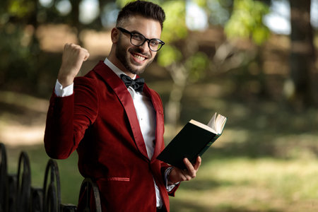 side view of an attractive businessman wearing red tuxedo holding a book and one fist up full of joy...