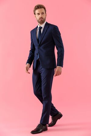 Pensive businessman curiously looking away while walking on pink studio backgroundの写真素材