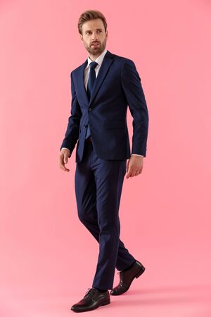 Pensive businessman curiously looking away while walking on pink studio background